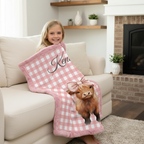 Child sitting on a couch with a pink checkered blanket featuring a cow design and the name 'Ken'.
