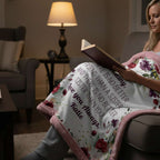 Woman reading a book with a floral blanket draped over her lap in a cozy living room.