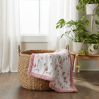 Woven basket with a pink and white blanket featuring animal prints in a room with plants and curtains.