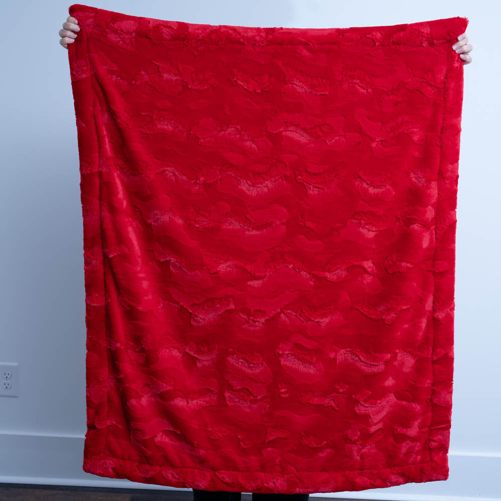 Red textured blanket being held up against a plain background