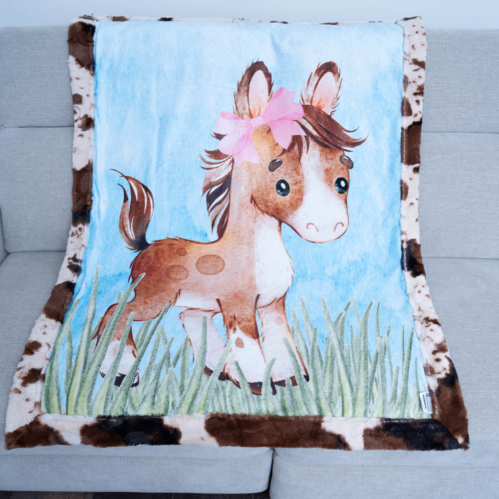 Blanket with a horse design featuring a pink bow on a gray couch.
