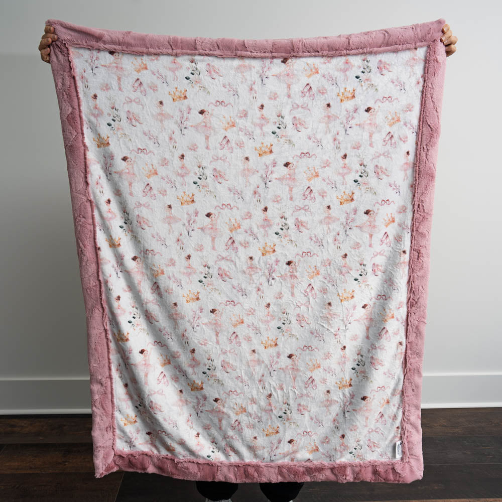 Floral patterned blanket with pink border held by a person against a white wall.