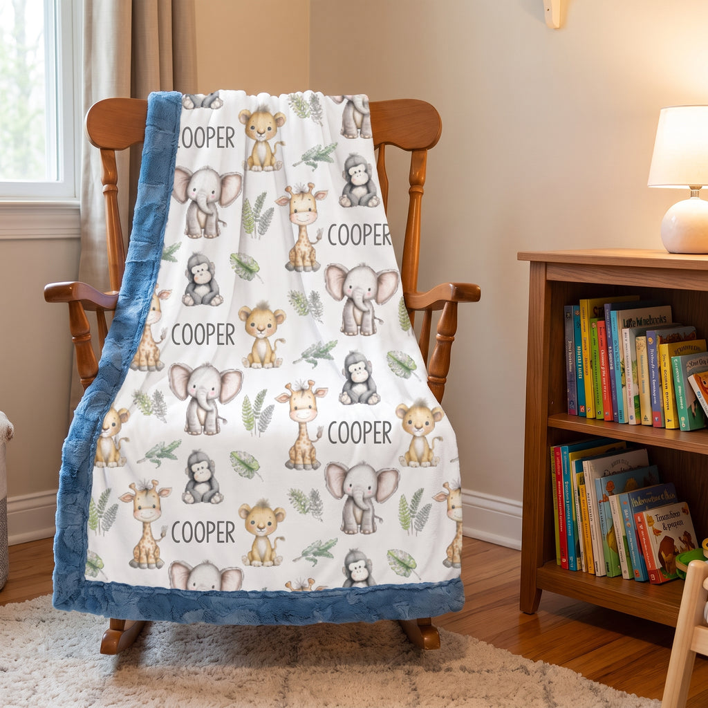 A personalized baby blanket with a blue minky fleece border and a white center printed with cartoon safari animals and the name 'COOPER', draped over a wooden rocking chair in a child's room.