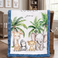 A personalized baby blanket with a blue minky border, featuring a white center printed with cartoon animals (giraffe, monkey, lion, elephant) and palm trees, with the name 'james' and the word 'COOLER' printed on it. The blanket is draped over a wooden chest in a nursery setting.