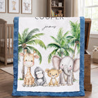 A personalized baby blanket with a blue minky border, featuring a white center printed with cartoon animals (giraffe, monkey, lion, elephant) and palm trees, with the name 'james' and the word 'COOLER' printed on it. The blanket is draped over a wooden chest in a nursery setting.