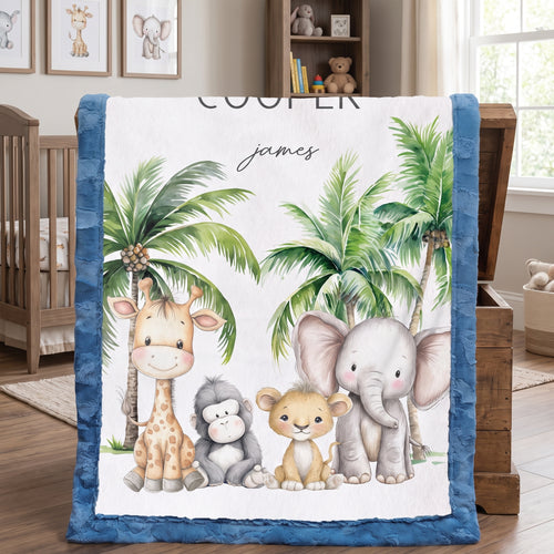 A personalized baby blanket with a blue minky border, featuring a white center printed with cartoon animals (giraffe, monkey, lion, elephant) and palm trees, with the name 'james' and the word 'COOLER' printed on it. The blanket is draped over a wooden chest in a nursery setting.