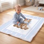 A baby sitting on a personalized baby blanket in a bright nursery. The blanket is light blue and white with a central illustration of a brown horse and the name 'SCOTTIE' printed in blue.