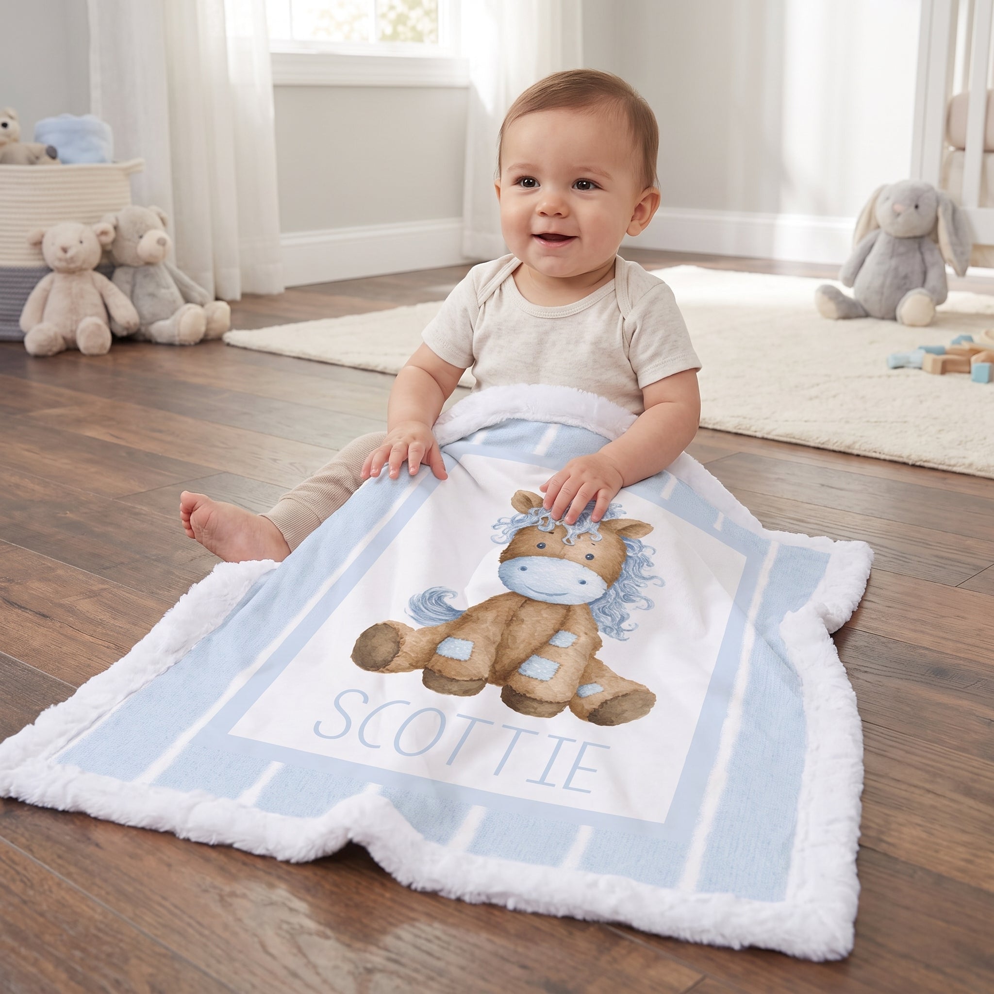 A baby sitting on a wooden floor in a nursery, wrapped in a personalized light blue and white blanket featuring a brown horse illustration and the name 'SCOTTIE'.