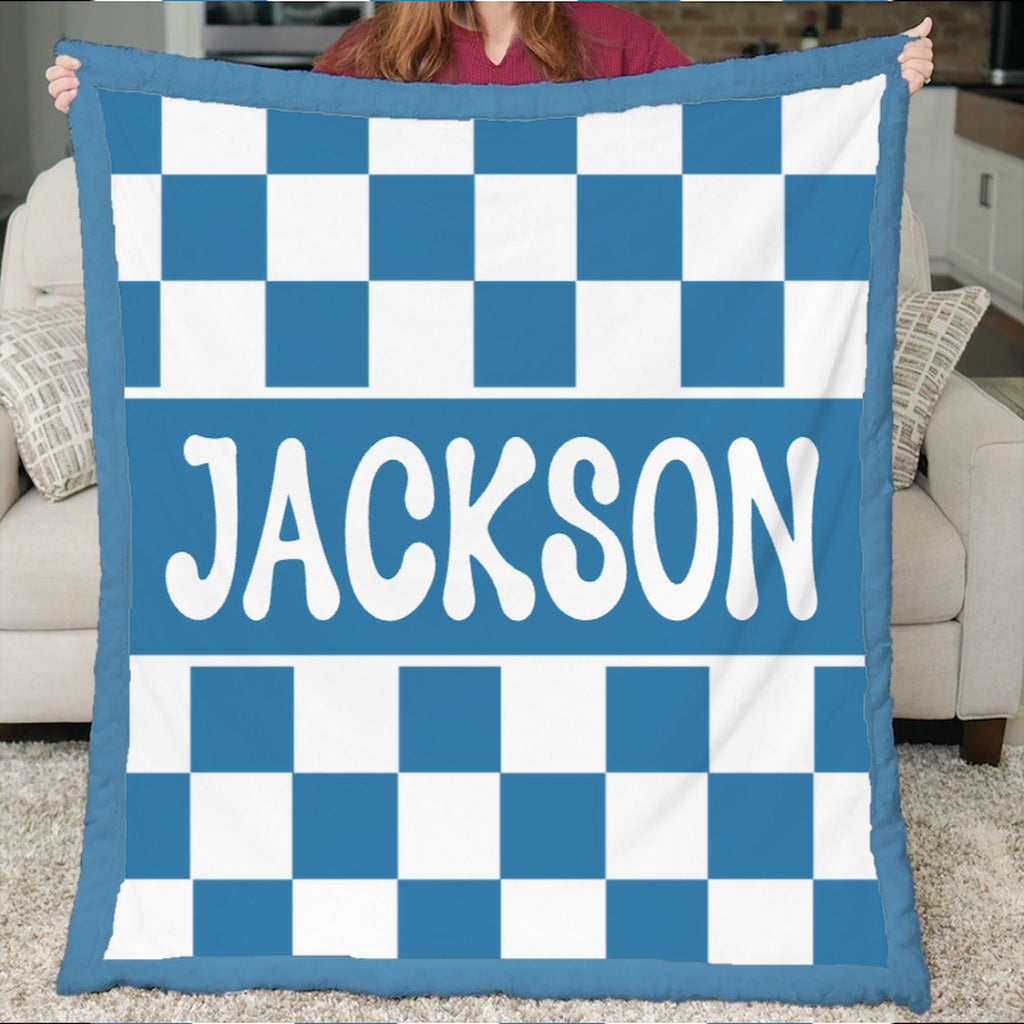 Blue and white checkered blanket with 'JACKSON' printed on it, held by a person in a living room.