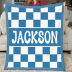 Blue and white checkered blanket with 'JACKSON' printed on it, held by a person in a living room.