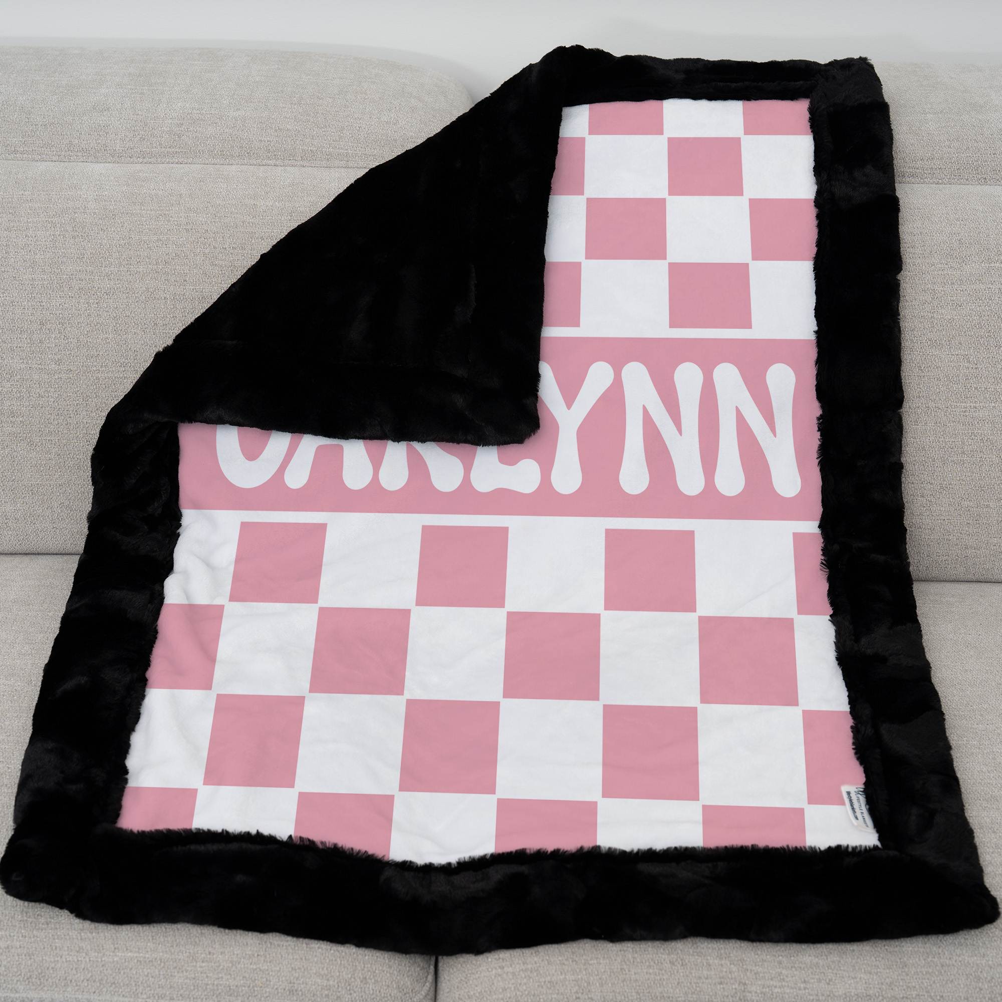 Pink and white checkered blanket with black border and 'Carlynn' text on a gray couch.