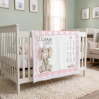 A personalized baby crib bedding set featuring a pink and white gingham border, a central white panel with a cute cartoon elephant wearing a pink bow, the name 'Eliana Elizabeth', numbers 1 through 12, and 'months' text, displayed on a white wooden crib in a styled nursery.