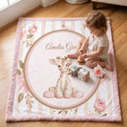 A baby girl's personalized play mat on a wooden floor, featuring a pink giraffe, pink roses, and the name 'Amelia Grace' in a central oval. A toddler is sitting on the mat playing with wooden toys.