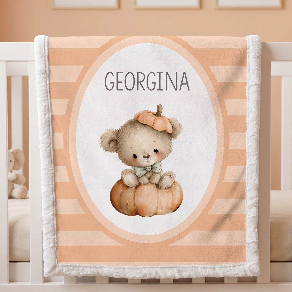 Personalized baby blanket with a cute teddy bear and pumpkin design, featuring the name 'GEORGINA' in the center, draped over a white crib.