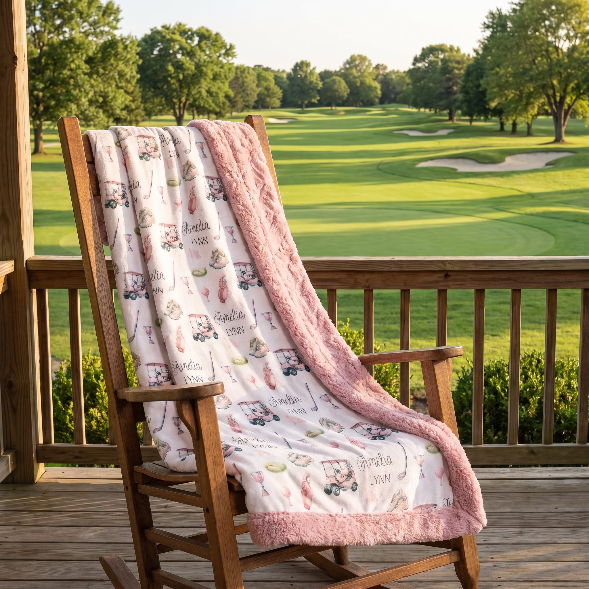 A pink and white golf-themed blanket draped over a wooden rocking chair on a porch, with a green golf course in the background.