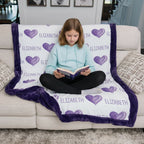Girl reading a book under a personalized blanket with purple hearts and name on a couch.