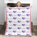 Child holding a blanket with purple hearts and the name 'Elizabeth' on it.