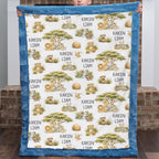A person holds up a minky quilt with a blue border and an all-over safari animal print featuring lions, giraffes, acacia trees, and the names 'KAYCEN LIAM'.