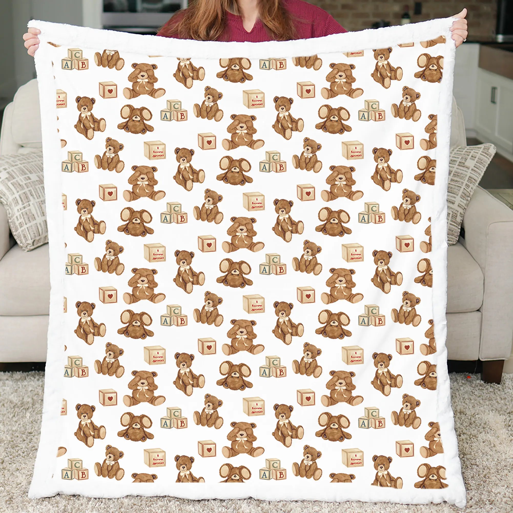 Person holding a blanket with teddy bear and elephant pattern in a living room.