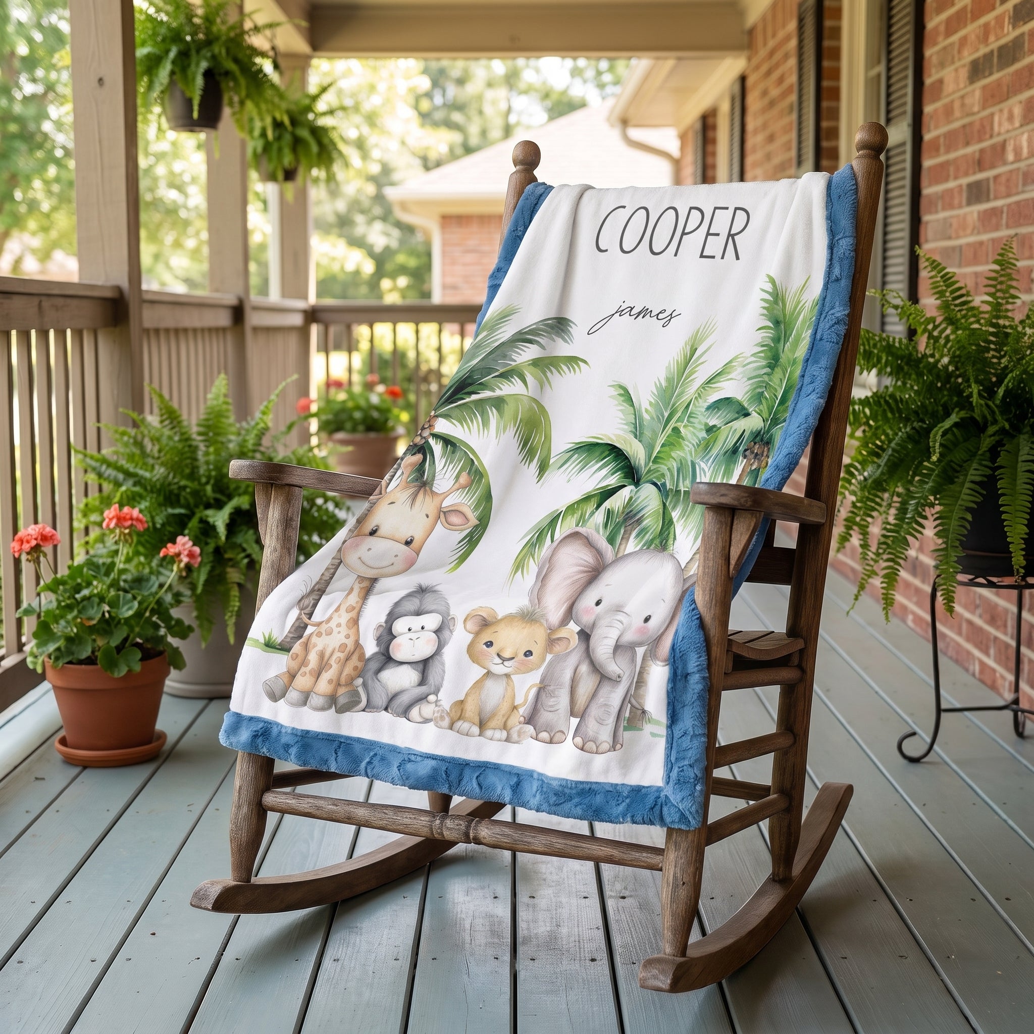 A personalized baby blanket with a safari animal design is draped over a wooden rocking chair on a porch. The blanket features a white background with illustrations of a giraffe, monkey, lion, elephant, and palm trees, bordered by a blue patterned edge.