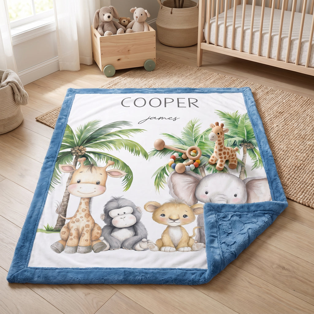 A personalized baby blanket with a blue border and a white center printed with safari animal illustrations including a giraffe, elephant, monkey, lion, and palm trees. The blanket is shown styled on a wooden floor in a nursery setting next to a crib and stuffed toys.