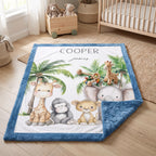 A personalized baby blanket with a blue border and a white center printed with safari animal illustrations including a giraffe, elephant, monkey, lion, and palm trees. The blanket is shown styled on a wooden floor in a nursery setting next to a crib and stuffed toys.