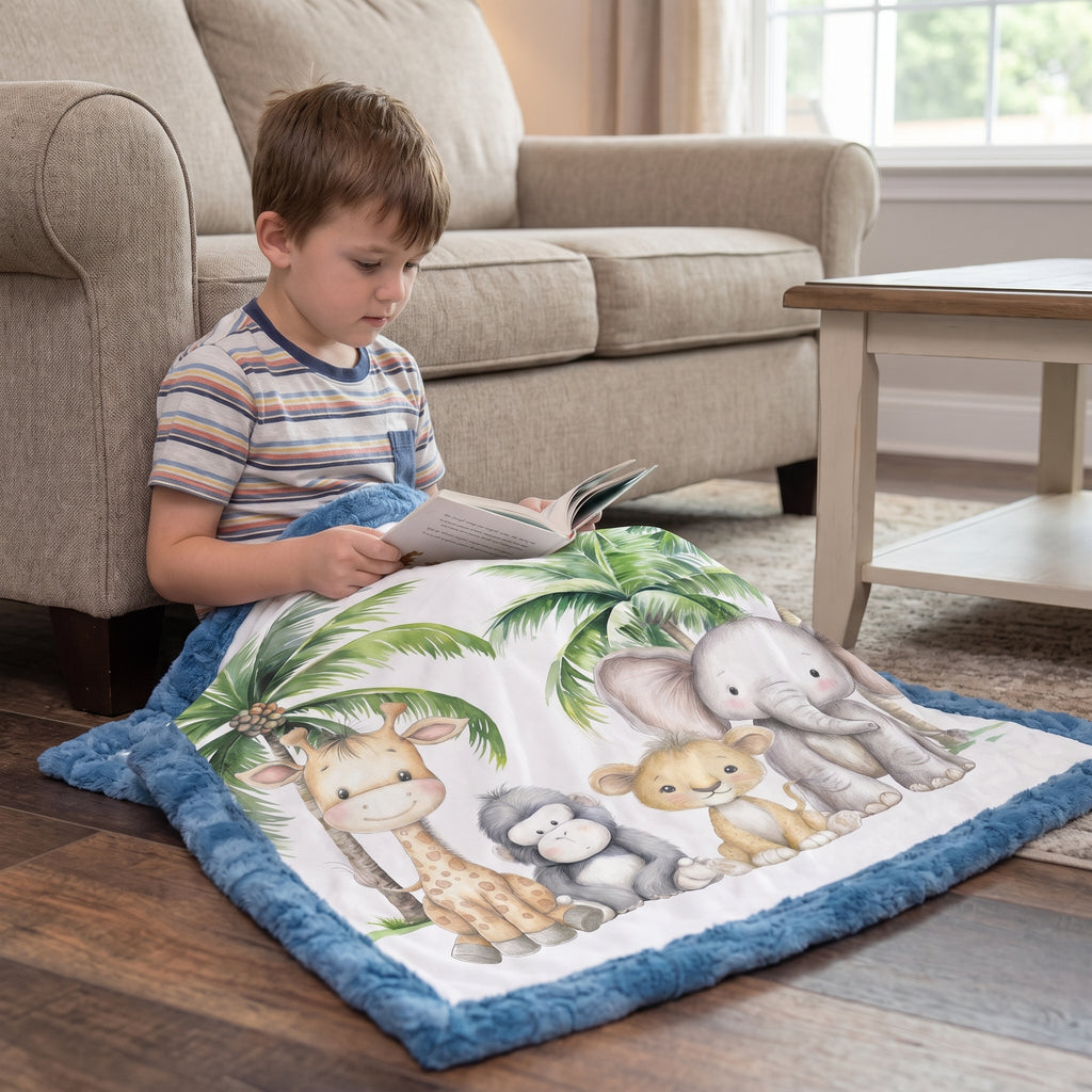 A young boy sits on a wooden floor in a living room, wrapped in a blue plush blanket featuring a safari animal print with a giraffe, elephant, monkey, and other jungle animals.