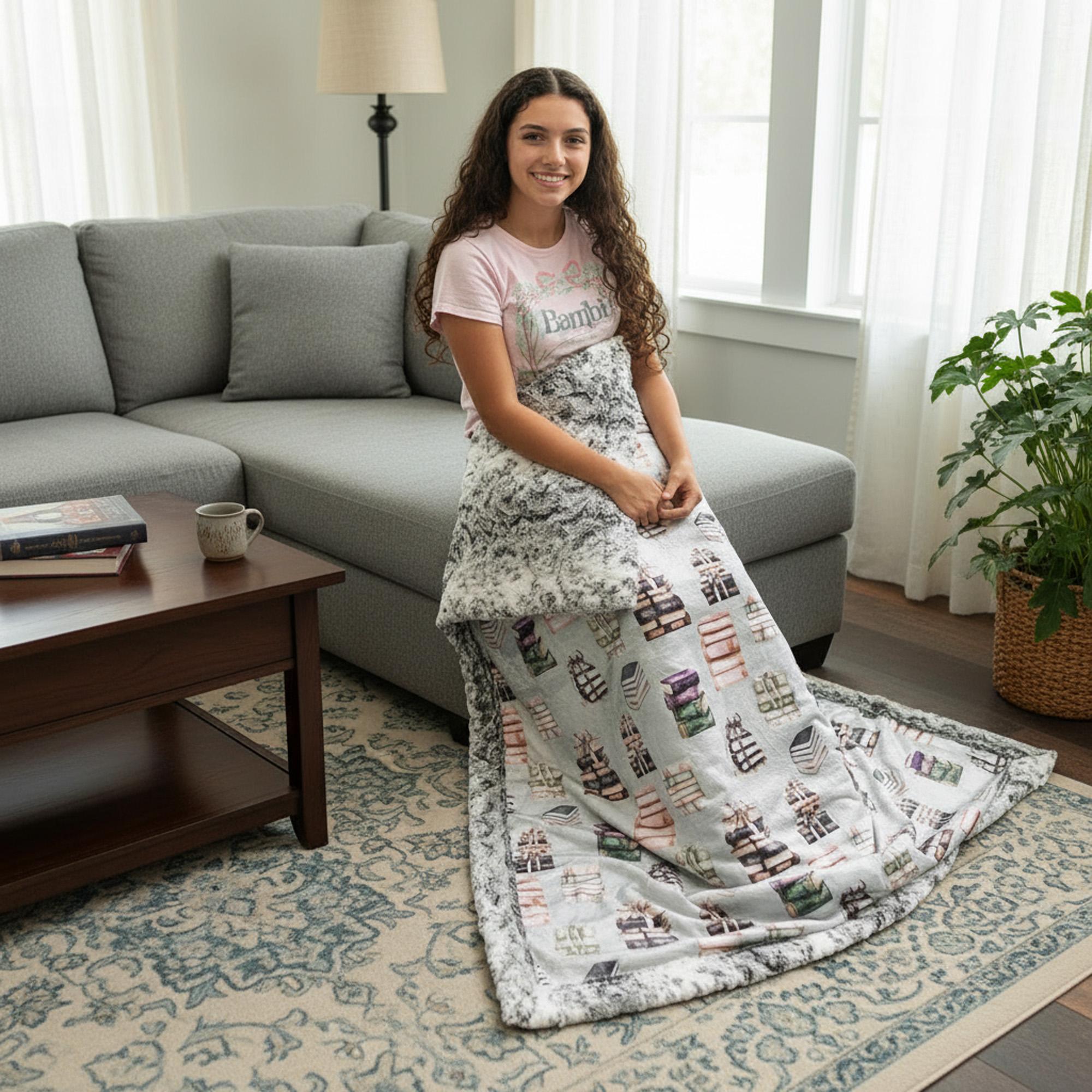 Woman sitting on gray sofa with folded book-themed minky blanket