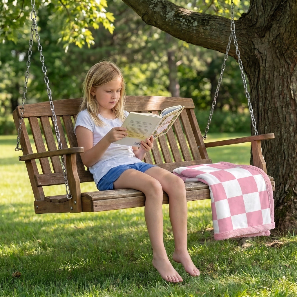 Pink and white checkered minky baby blanket draped on porch swing beside girl reading outdoors