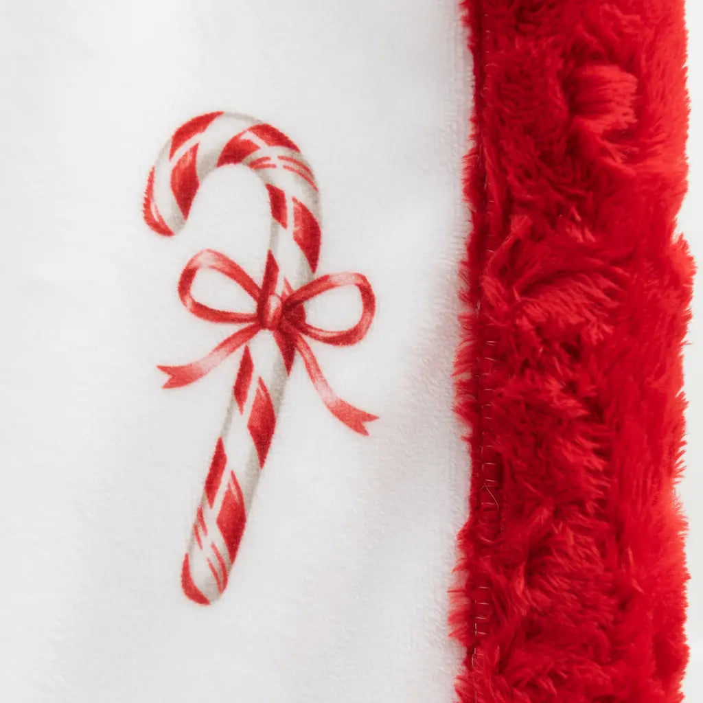 Red and white candy cane with a bow next to a red textured blanket on a white background
