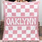 Person holding a pink and white checkered blanket with 'OAKLYNN' printed on it.