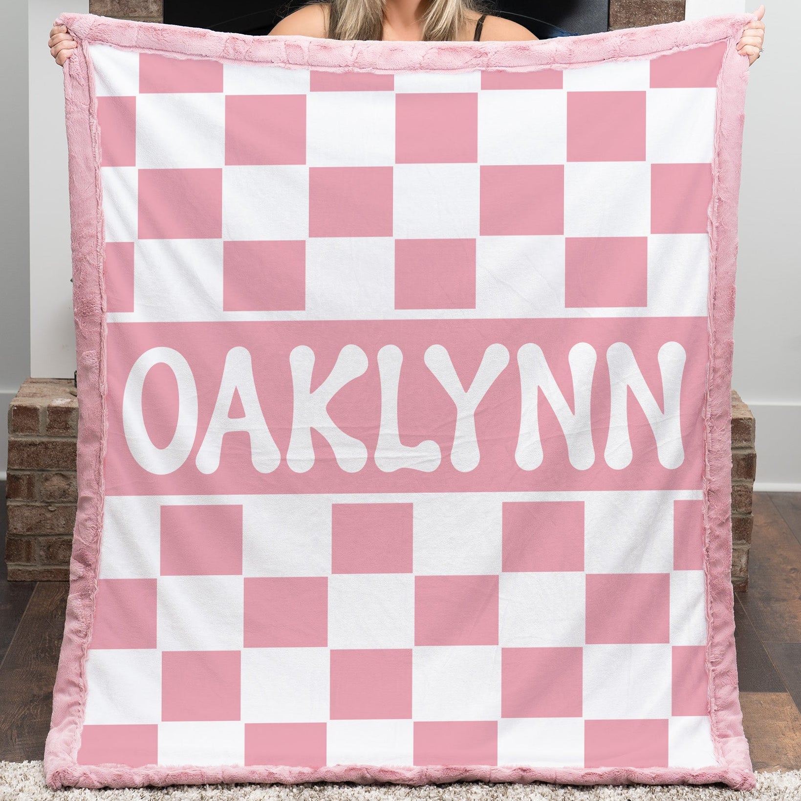 Person holding a pink and white checkered blanket with 'OAKLYNN' printed on it.