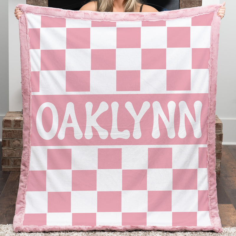 Person holding a pink and white checkered blanket with 'OAKLYNN' printed on it.
