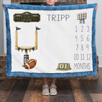 A person holds up a custom football-themed blanket featuring a white center with a blue border, printed with a football goal, football, scoreboard, stadium lights, and a 12-month countdown for the name TRIPP.