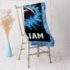 Close-up of personalized football minky baby blanket with blue splash design on a rustic chair