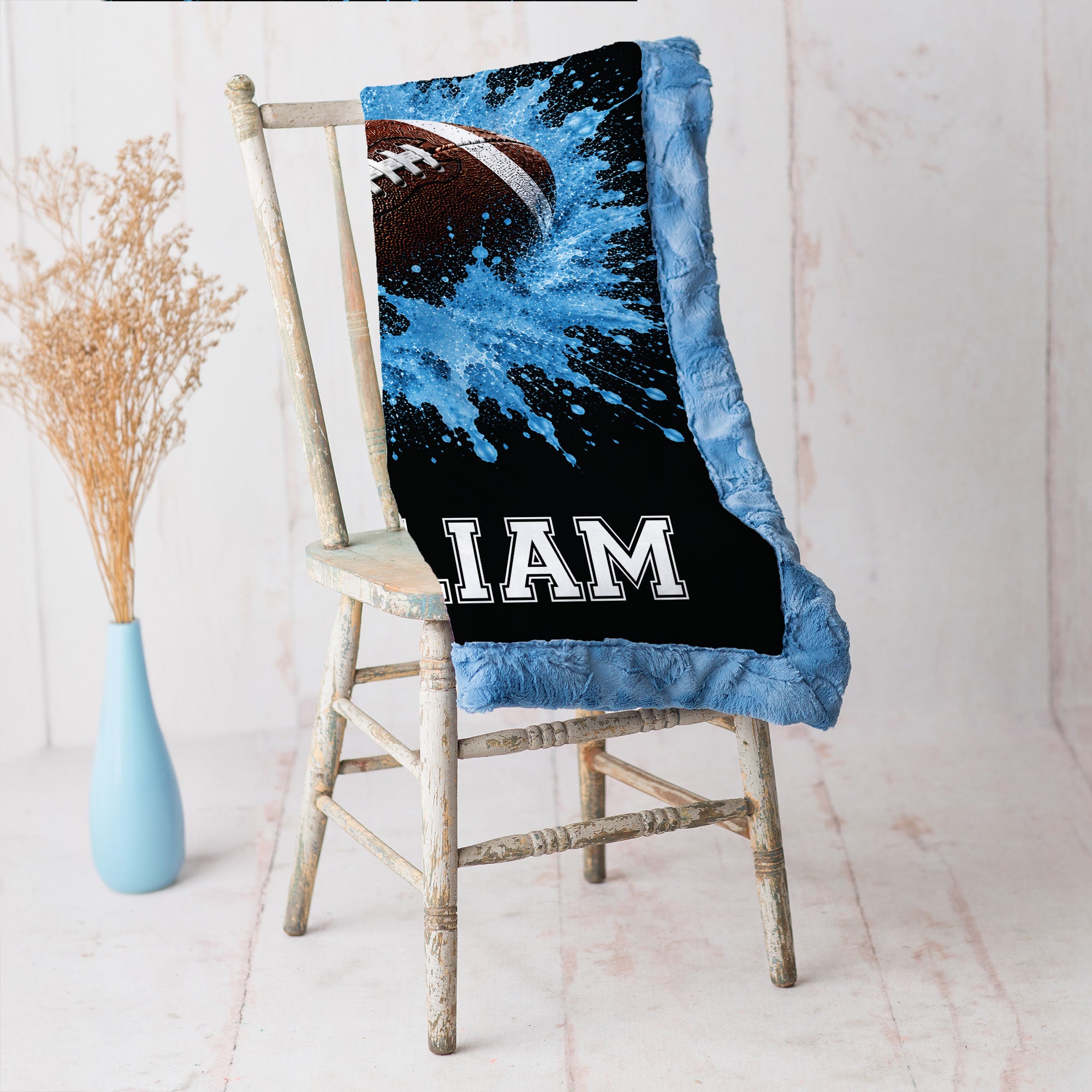 Close-up of personalized football minky baby blanket with blue splash design on a rustic chair