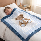 A child sleeping in bed under a personalized baby blanket featuring a teddy bear design and the name 'CHRISTOPHER'.