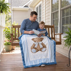 A father and child sit on a wooden porch swing reading a book, with a personalized blue and white blanket featuring a teddy bear and the name 'CHRISTOPHER' draped over them.
