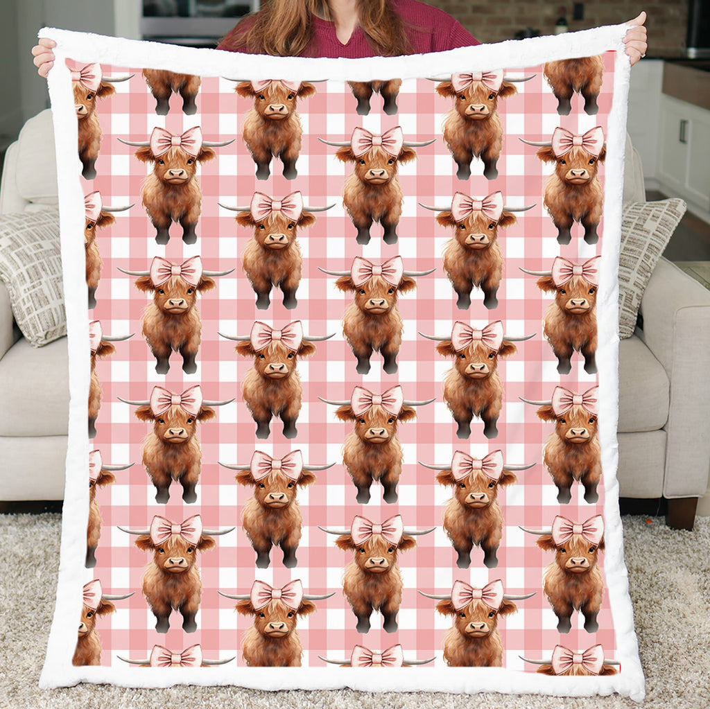 Blanket with Highland cow pattern on a pink checkered background held by a person.