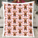 Blanket with Highland cow pattern on a pink checkered background held by a person.