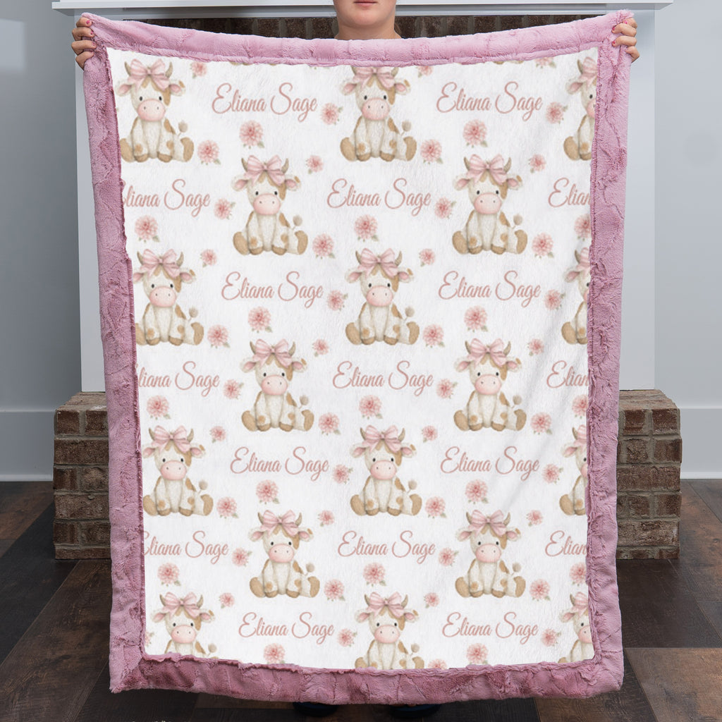 Personalized highland cow minky baby blanket with dusty pink fur trim, held up by fireplace
