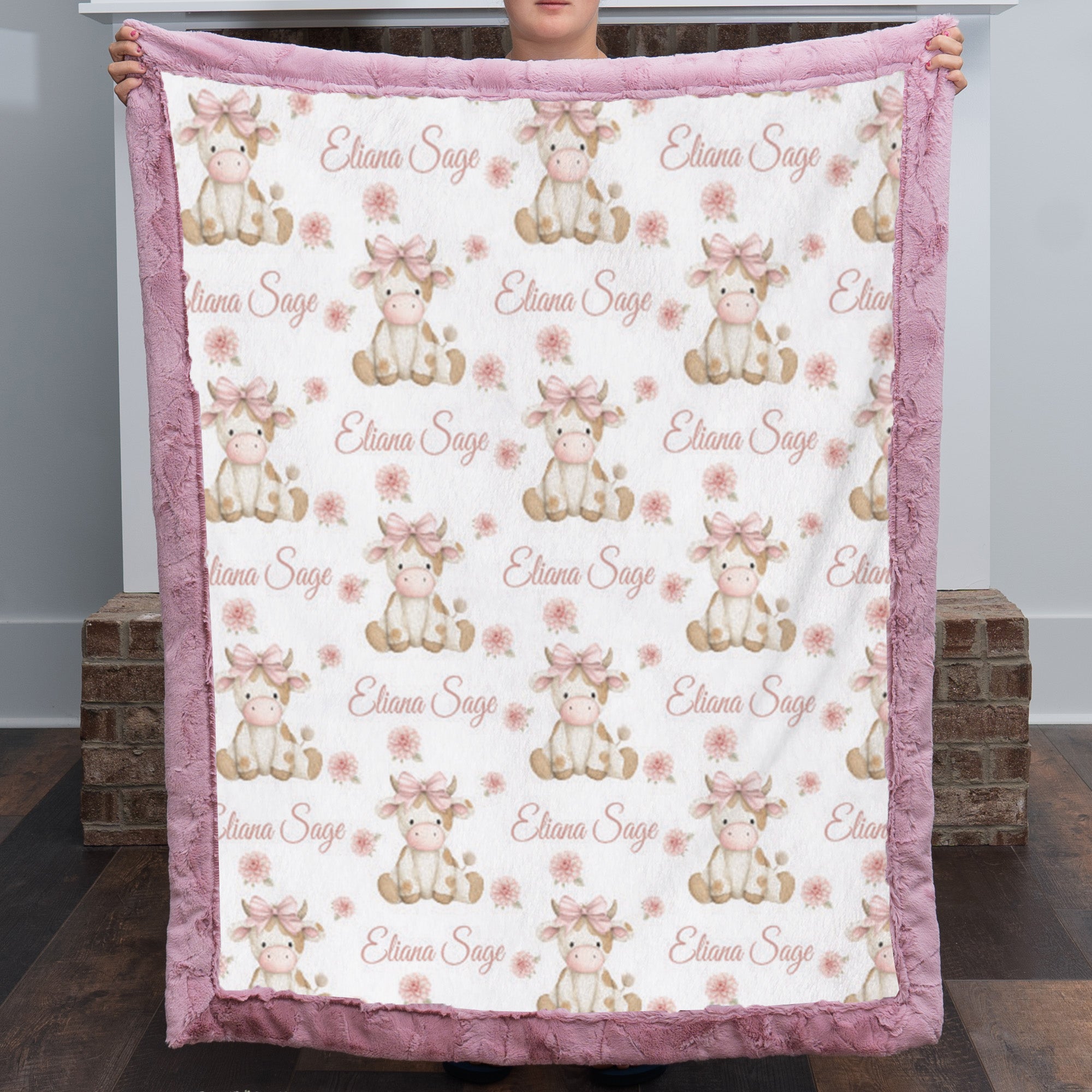 Personalized highland cow minky baby blanket with dusty pink fur trim, held up by fireplace