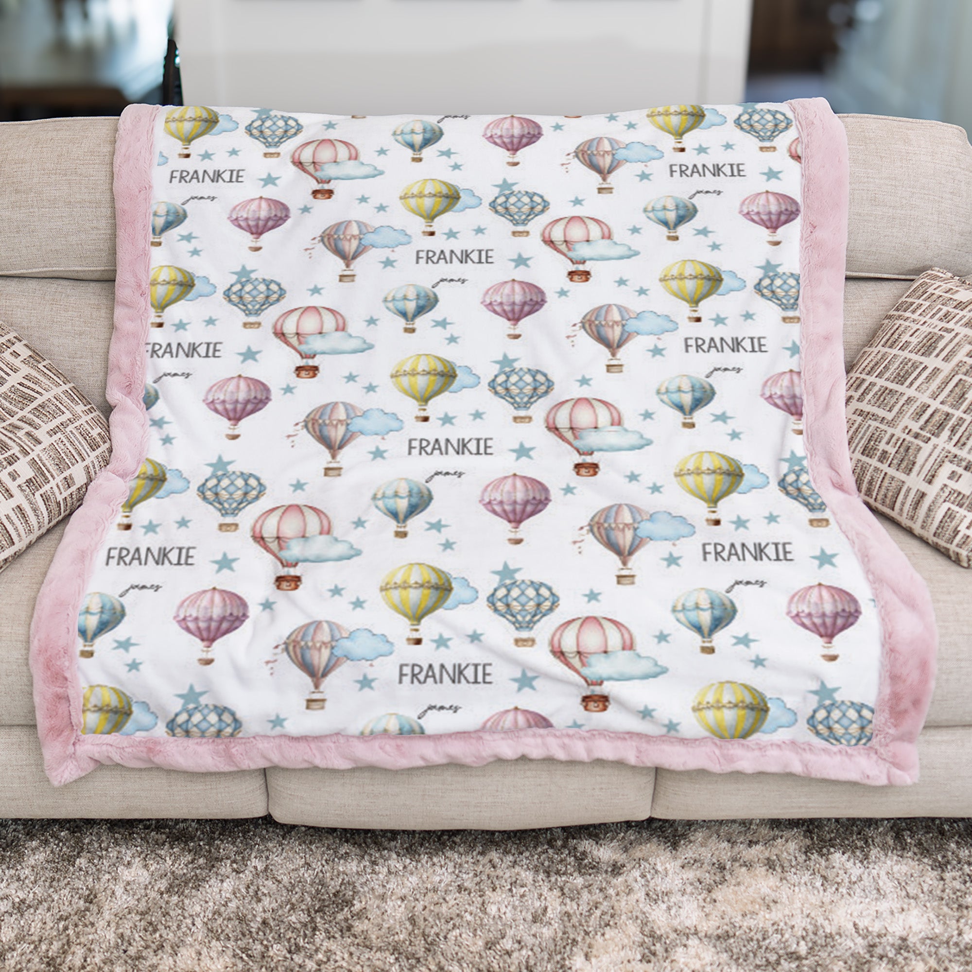 Hot air balloon personalized baby blanket with pink minky trim laid flat on sofa