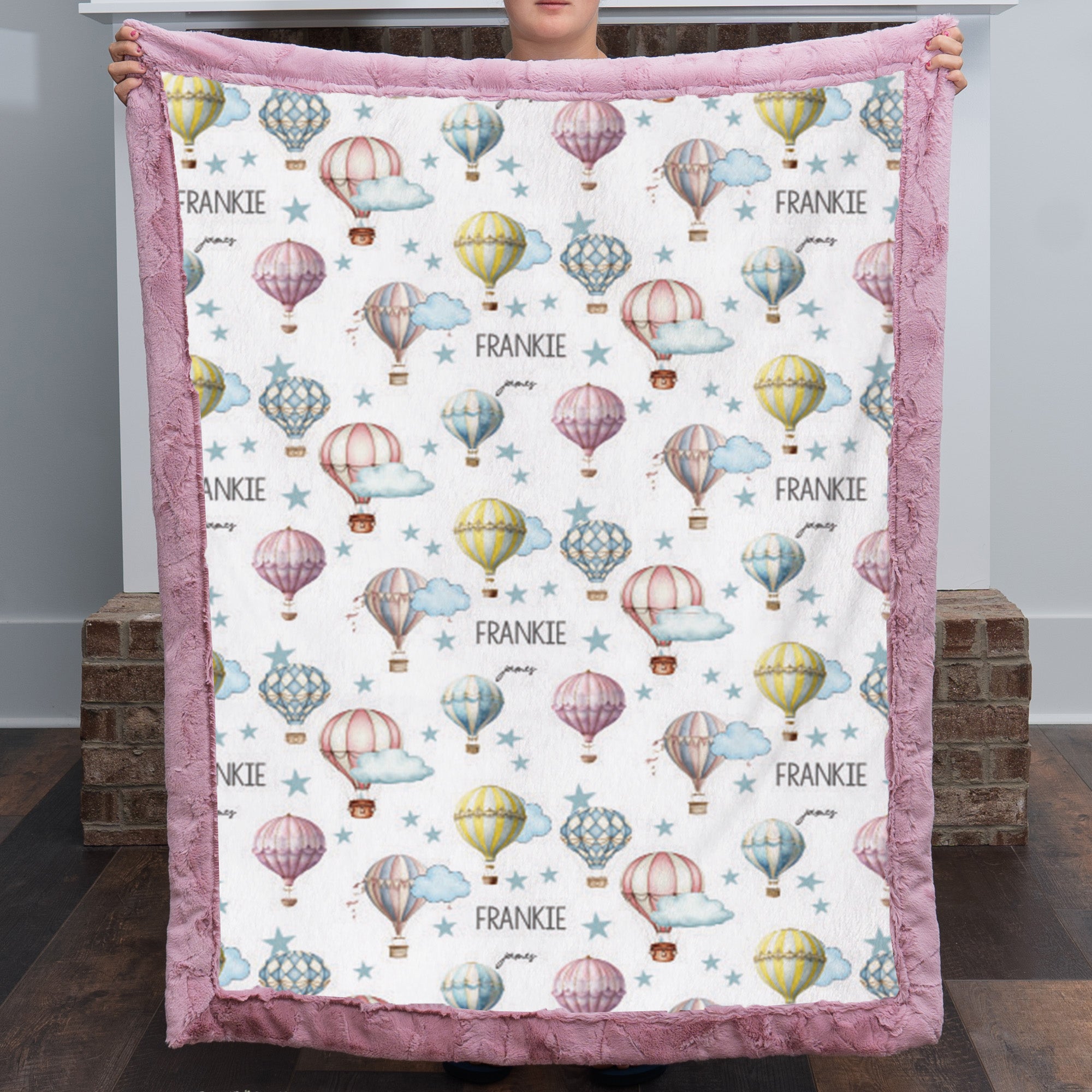 Woman holding up personalized hot air balloon baby blanket with pink minky border