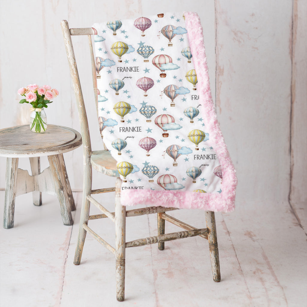 Personalized hot air balloon baby blanket with pink minky border draped on vintage chair
