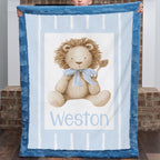 A person holds up a personalized plush blanket featuring a teddy bear design and the name 'Weston' printed at the bottom. The blanket has a blue border and a light blue and white striped center with a beige teddy bear wearing a blue bow tie.
