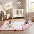 A pink and white baby quilt with a plush elephant design and the text 'BONSAI ARETH' is spread out on a wooden floor in a styled nursery. A gray plush elephant toy sits on the corner of the quilt, with a white crib, rocking chair, and window in the background.