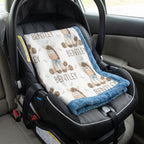 A personalized baby car seat blanket with a teddy bear pattern and the name 'BENTLEY' printed repeatedly, laid out inside a black infant car seat on a car seat.
