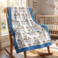 A plush baby blanket with a blue border and a white center printed with teddy bear illustrations and the name 'BENTLEY' is draped over a wooden rocking chair in a softly lit nursery.