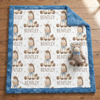 A personalized minky blanket with a blue plush border, featuring a white center printed with brown cartoon horses, the name 'BENTLEY', and small cross motifs. A matching plush toy is placed on the blanket, which is laid out on a wooden floor.